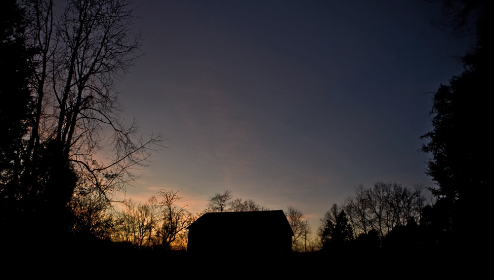 silhouette of barn and surrounding trees during sunset